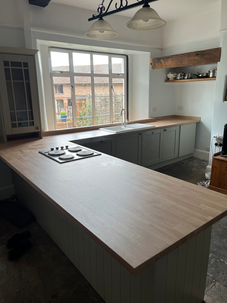 Modern kitchen with new wooden worktops, sage green cabinets, and large window.
