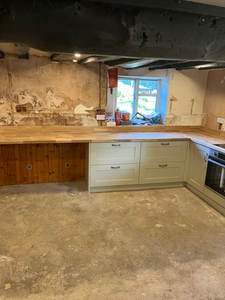 Kitchen renovation with light green cabinets, wooden worktops, and exposed walls.