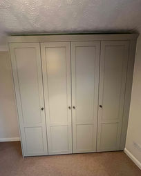 Modern light grey four-door fitted wardrobe in a bedroom.