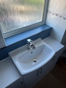 Modern white ceramic sink with chrome faucet, blue window shelf, tiled wall.