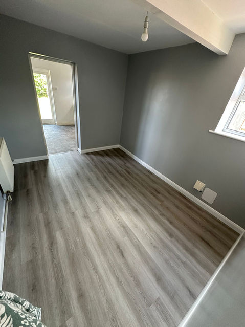 Bright empty room with light grey laminate flooring, freshly painted grey walls.