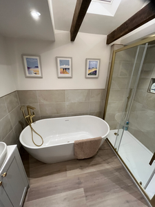Modern bathroom with white freestanding tub, glass shower, brass fixtures, art.