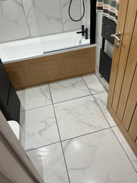 Modern bathroom with white marble-effect floor and wall tiles, wooden bath panel.