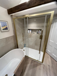 Modern bathroom with gold framed shower, white tub, and CROYDE picture.
