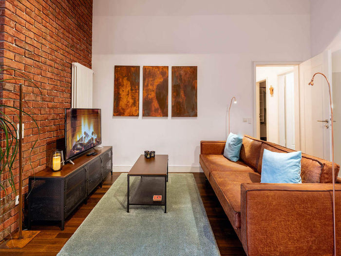 A living room with brick, dark parquet and a brown leather couch.