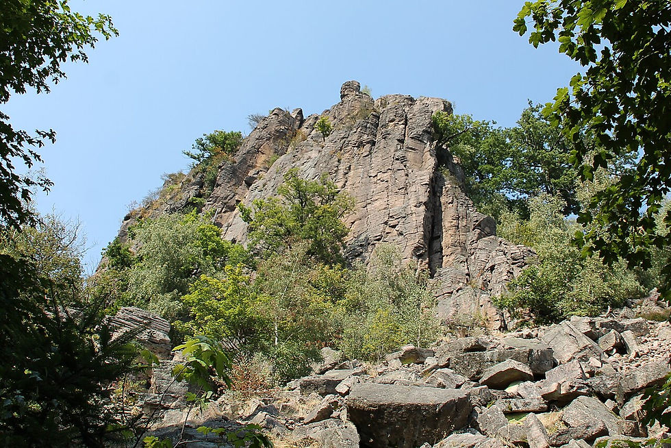 Felsiger Berg mit Bäumen und Geröll unter blauem Himmel, ruhige Naturlandschaft.