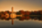 Monument reflected on calm water with trees and soft orange sky