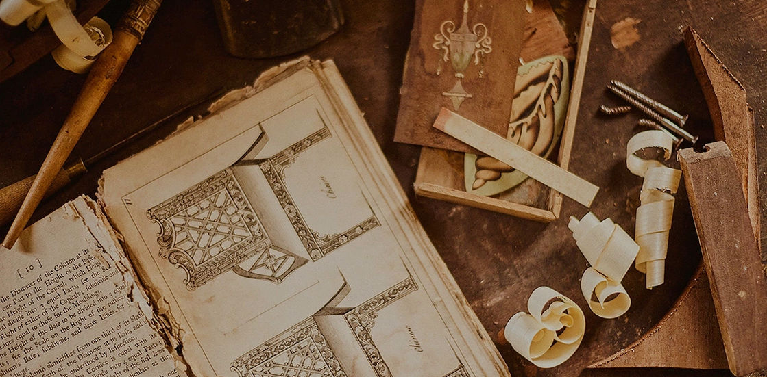 Open book with blueprints, tools, wood shavings, and a small wooden box.