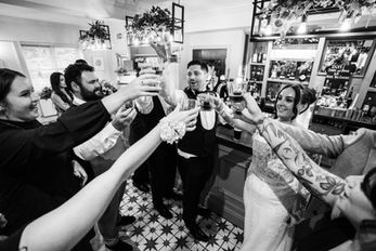 Group of people toasting drinks at a bar, celebratory moment captured, Wedding Photography in leeds and yorkshire.