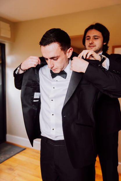 Groom adjusting his suit, with the help of his best man.