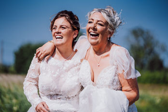 Two brides laughing together in wedding dresses, Claire & Lisa, sunny day.