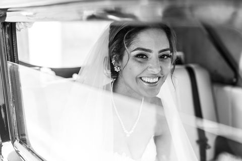 Smiling bride in wedding dress sitting in car, ready to get married