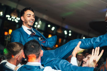 Groom being lifted in the air by friends, smiling, celebrating a wedding