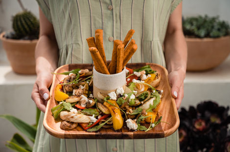 Woman holding a wooden platter of grilled vegetables and breadsticks