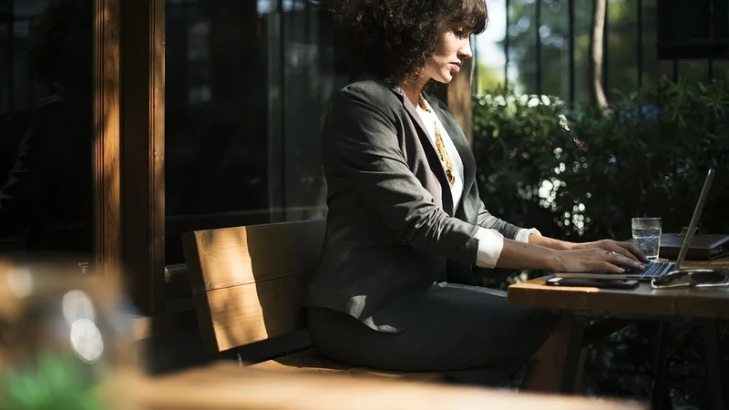 a woman in a suit sits on a bench using a laptop