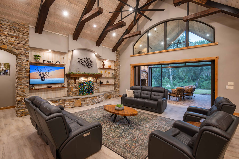 Cozy living room with black sofas, stone fireplace, TV, and "Family" sign. Large windows show a forest view. Warm, welcoming ambiance. Mastrosimone Construction custom luxury living room Lake County Florida