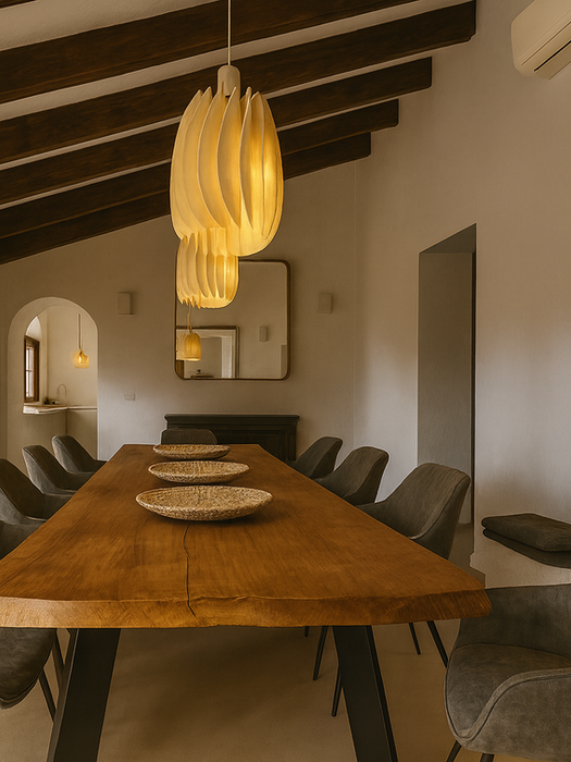 Elegant Mediterranean dining room with long solid wood table, gray upholstered chairs, pendant lights, and exposed wooden ceiling beams – Can Ferragut Mallorca.