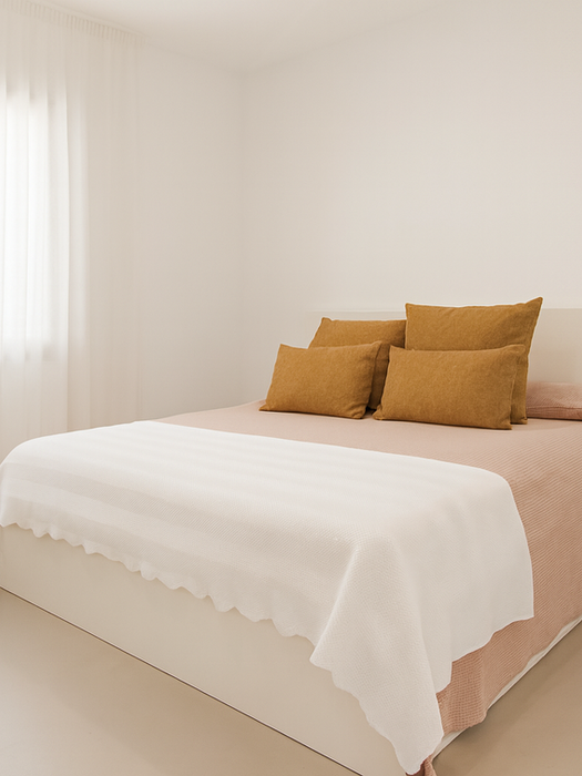Minimalist bedroom with blush bedspread, mustard accent pillows, white throw blanket, and sheer curtains allowing natural light – Can Ferragut Mallorca.