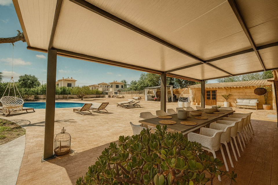 Covered outdoor dining space with long table, white chairs, hanging chair, poolside loungers, and Mediterranean courtyard setting – Can Ferragut Mallorca.