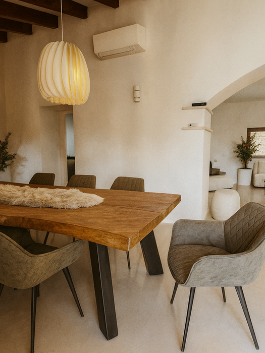 Rustic Mediterranean dining room with solid wood table, upholstered chairs, pendant lights, and arched opening to living room – Can Ferragut Mallorca.