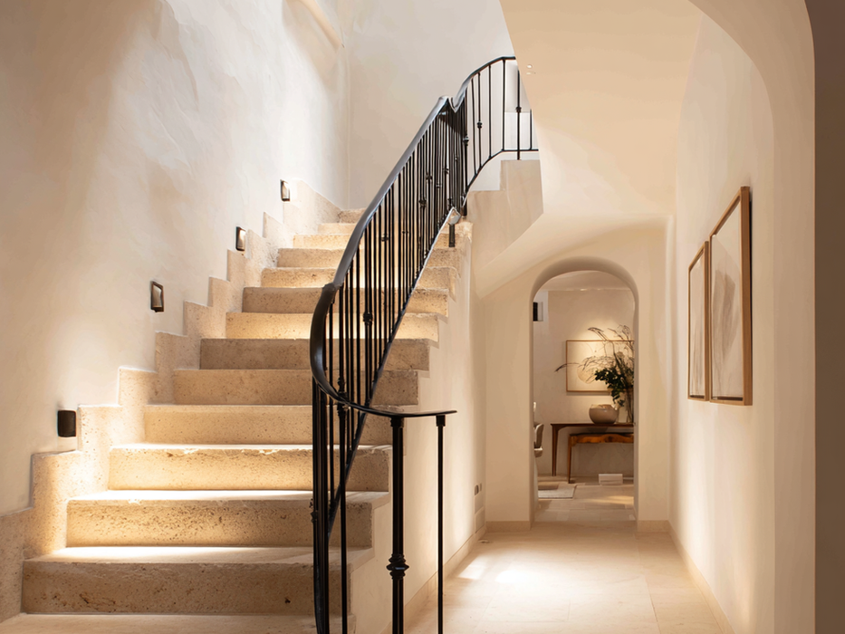 Curved staircase with minimalist design and warm lighting in Mediterranean villa interior.