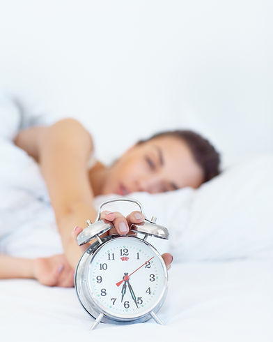 5 more minutes.... Shot of a sleepy young woman reaching out to turn off her alarm clock..