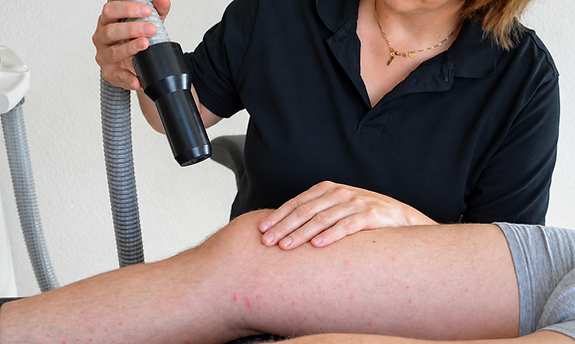 Eine physiotherapeutische Behandlung am Knie mit einer lokalen physikalischen Anwendung. Die Therapeutin positioniert das Handstück gezielt über dem Knie und kontrolliert gleichzeitig die Behandlung.