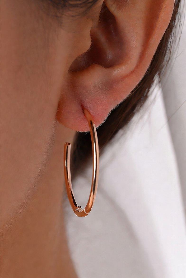 Close-up of a rose gold hoop earring on a person's ear.