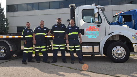 Four tow truck workers standing next to a tow truck, Towing Services.