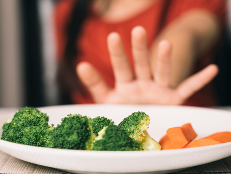 A girl denying a plate of food: broccoli and carrots
