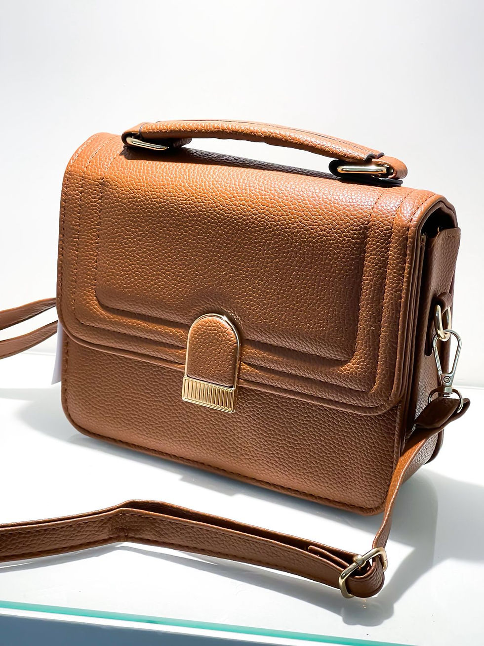 Miniatura: Bolsa transversal caramelo de couro sintético texturizado com alça de mão e fecho frontal vertical dourado.