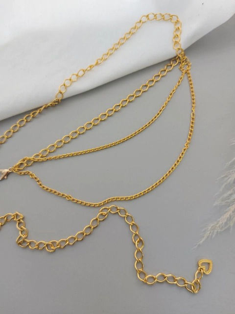 Cinto de corrente dourada com três voltas de elos de diferentes espessuras e alongamento, sobre um fundo cinza e branco.