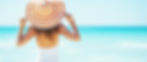 woman on beach in an orange and white striped large sunhat, looking out to the ocean - image banner for the FAQs page on Beach Beds Tanning website