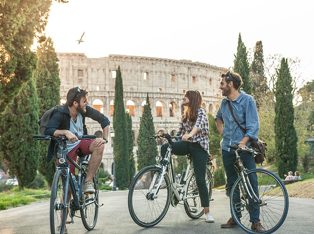 Three young friends tourists with bikes in colle oppio park in front of colosseum on road