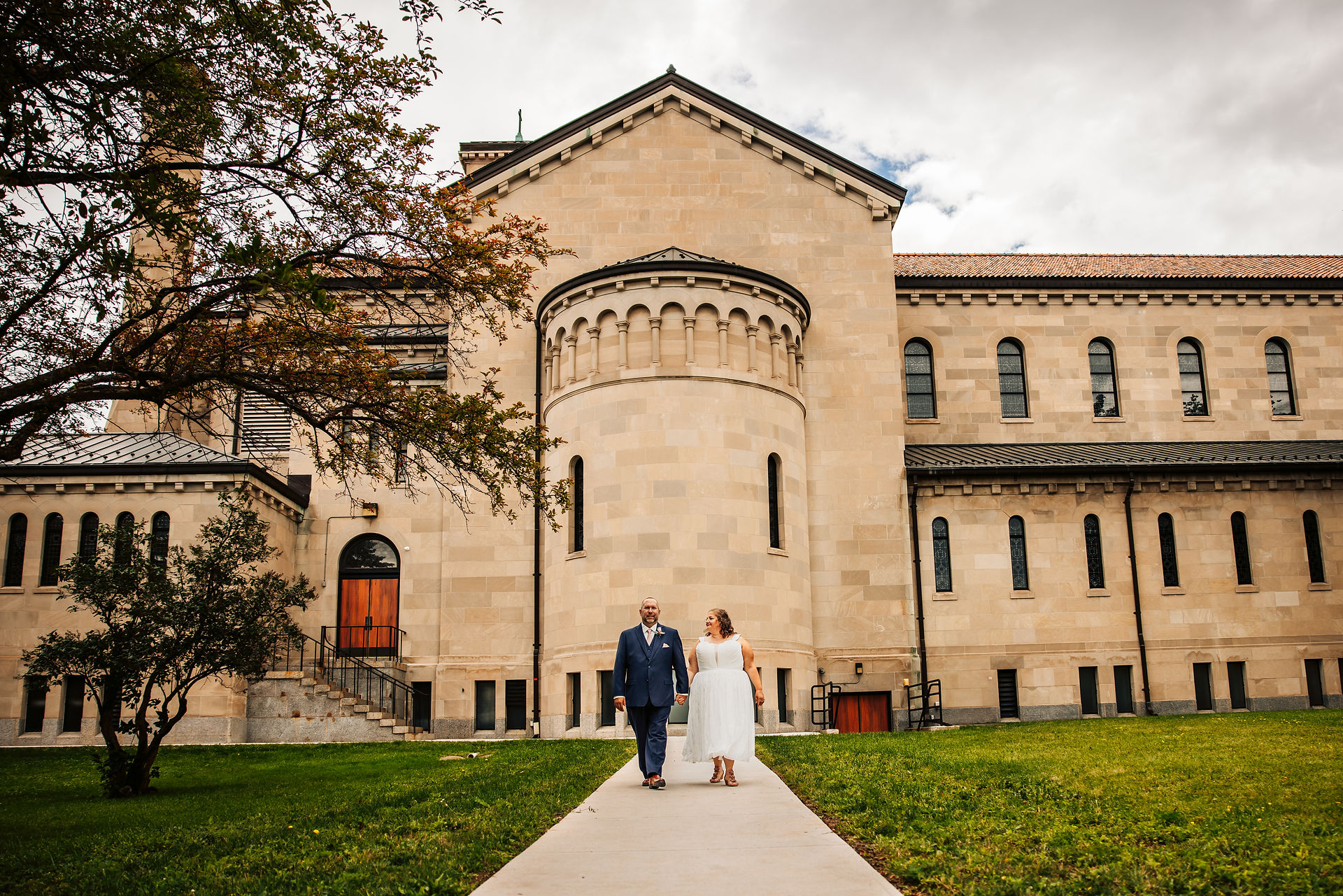 A bride and groom walking on a path outside of a Cathedral