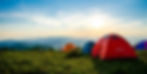 Morning view of a camping site in Pune, with tents arranged on the grass, bathed in soft sunlight. The surrounding hills and trees are covered in dew, and the sky is clear with a fresh, serene atmosphere.