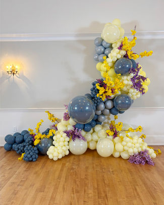 Large diagonal organic balloon wall garland featuring navy and yellow balloons with floral accents.