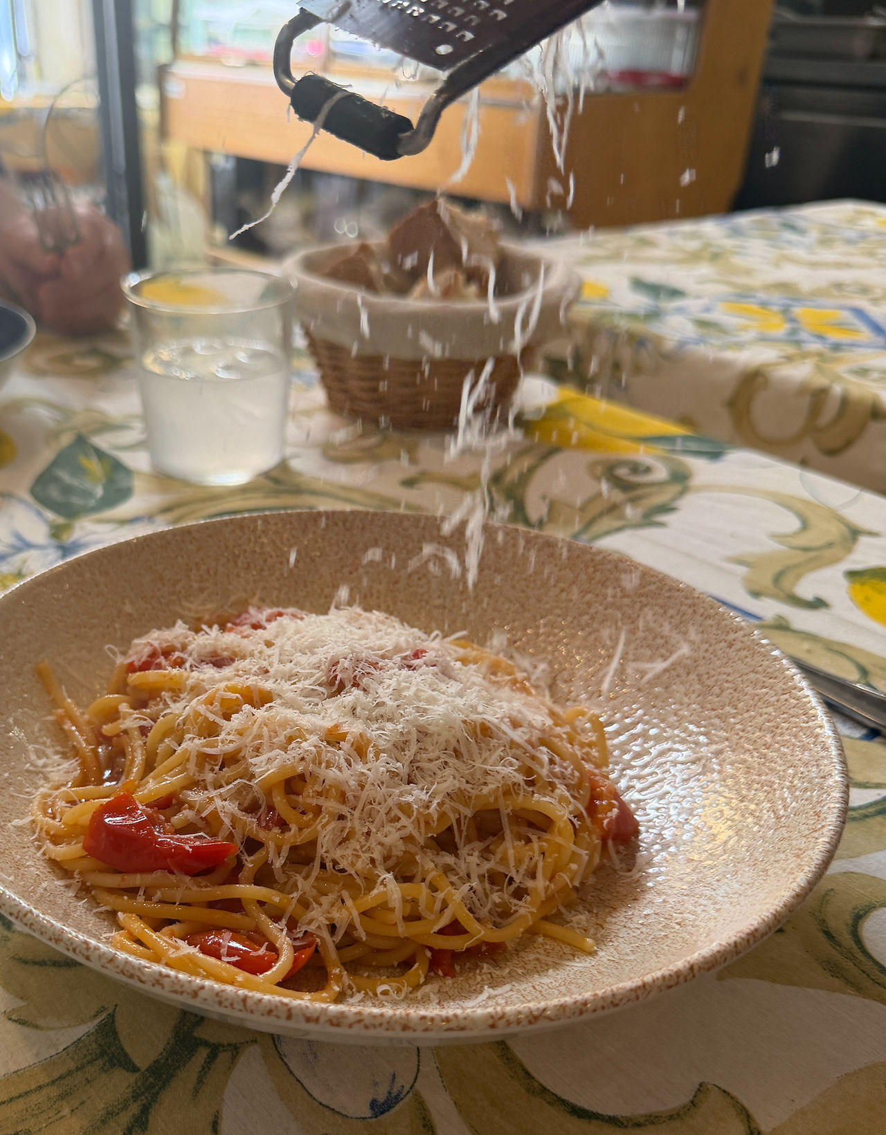 Bowl of pasta with tomatoes and someone grating parmesan cheese onto it