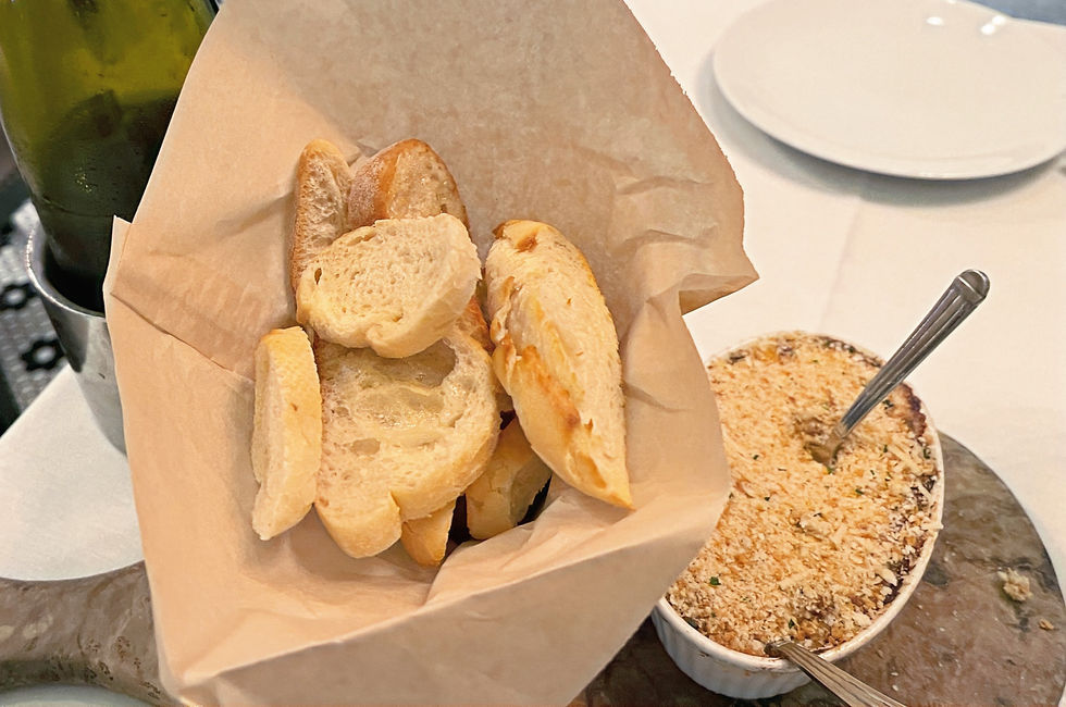 basket with brown paper and sliced baguette with a white bowl of dip 