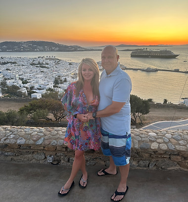 couple in Mykonos with the city and ocean with sunset behind them