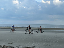 Two girls on bikes on the beach with ocean in background