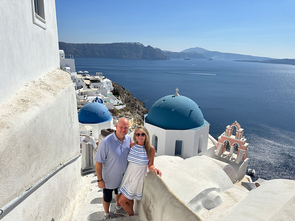 Couple standing on white stairs with blue dome roof and ocean behind them in Santorini Greece