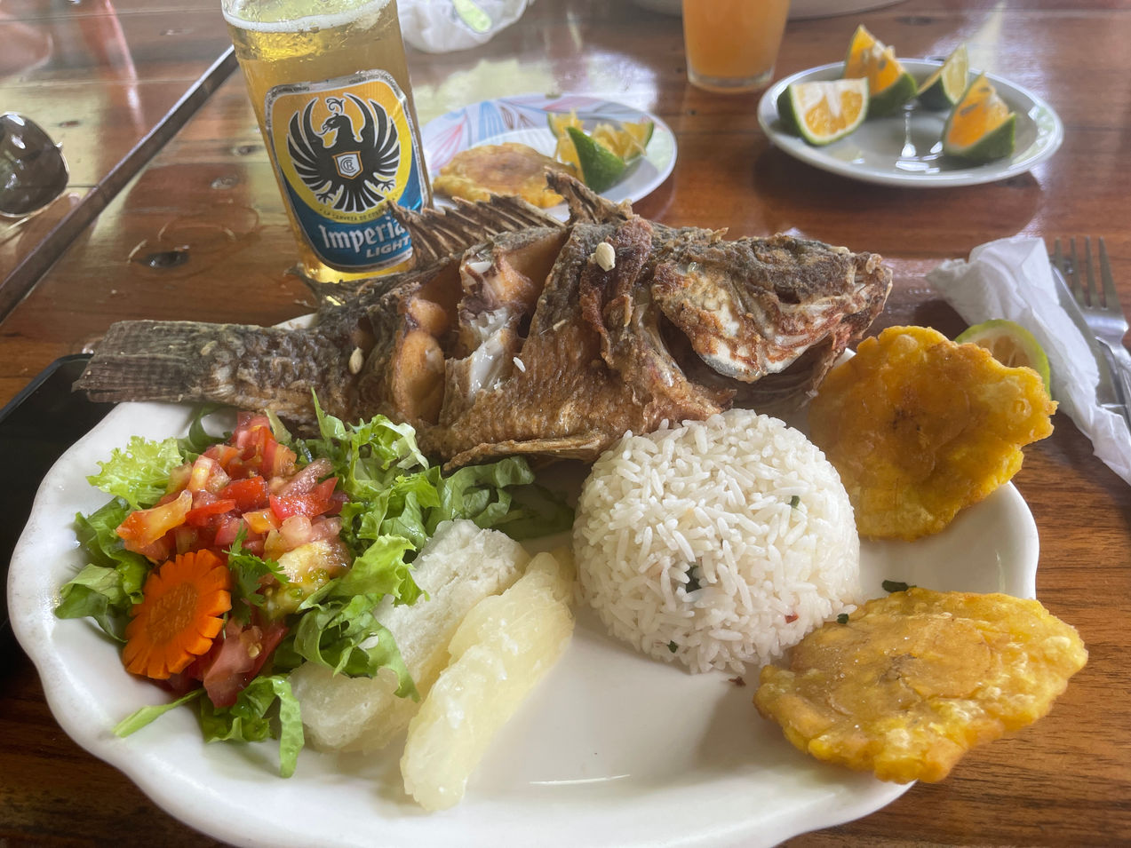 Whole Fish Tilapia with rice and salad and two fried plantains on a white plate