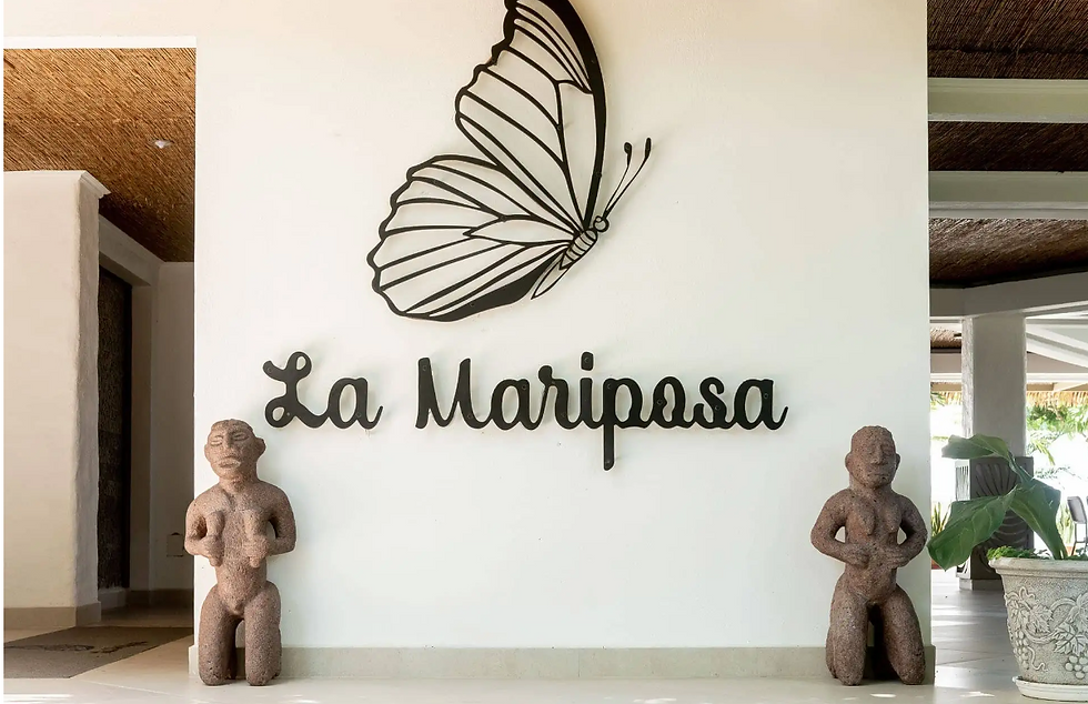 Entrance to La Mariposa resort with two statues and a large butterfly on a white stone wall