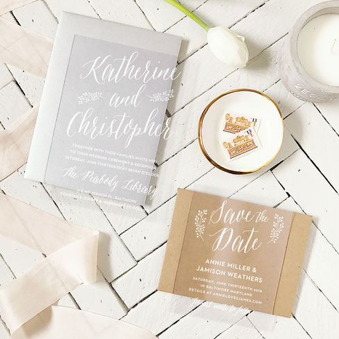 wedding flat lay of an acrylic wedding invitation and save the date with a tulip flower, a small white dish with stamps, white ribbon and a candle