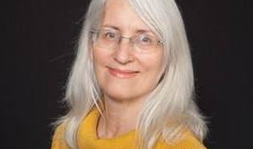 Smiling woman in gold sweater with glasses and beautiful grey hair