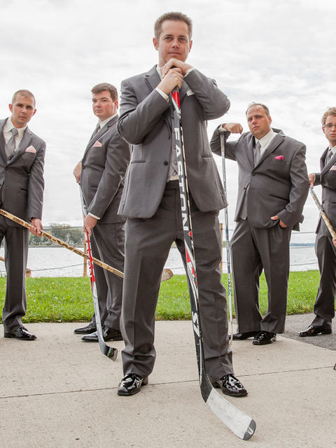 Groomsman Portrait with 6 groomsmen in formal grey suits posing with hockey sticks.