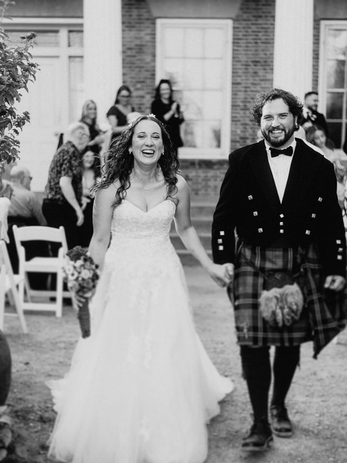A black and white photo of the bride and groom smiling with joy as their walk down the aisle after their wedding.