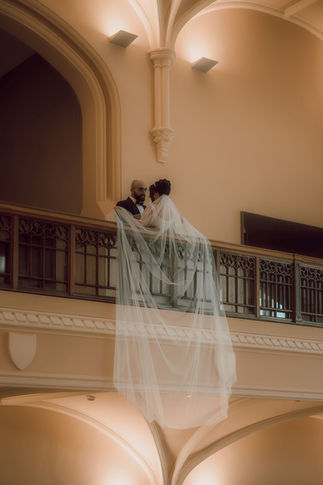 Bride and groom kissing on an upper balcony railing with a long flowing veil draped over the ledge at the Canadian Museum of Nature in Ottawa.