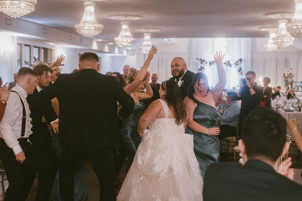 Wedding reception scene with guests dancing joyfully under chandeliers. The bride in a white dress, others in teal, lively and festive atmosphere.